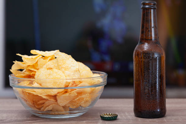 A bowl of chips and a beer in front of a TV stock photo