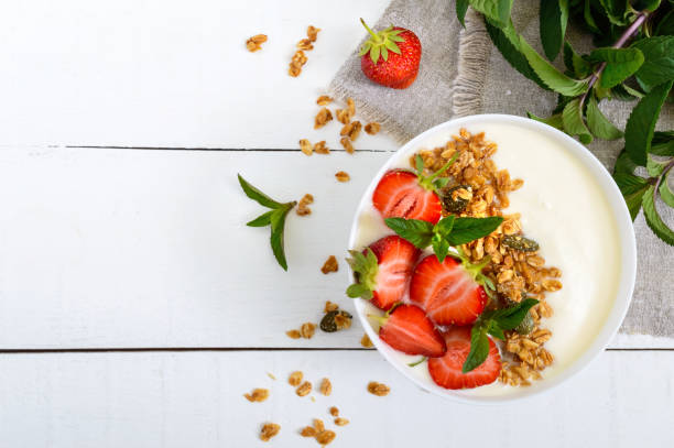 A bowl of dietary fitness breakfast: yogurt, granola, fresh strawberry, mint on a white wooden background. Proper nutrition. Top view. A bowl of dietary fitness breakfast: yogurt, granola, fresh strawberry, mint on a white wooden background. Proper nutrition. Top view. strawberry smoothie stock pictures, royalty-free photos & images