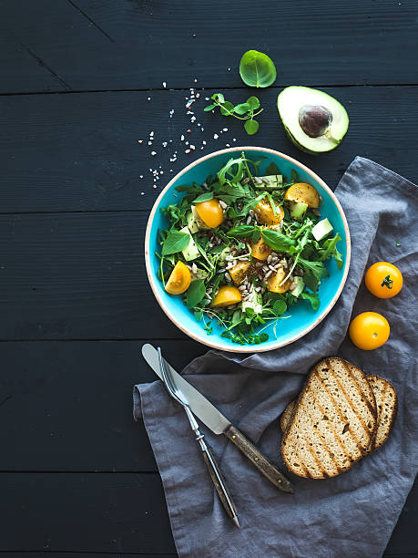 Bowl of green salad with avocado, arugula, cherry tomatoes and Bowl of green salad with avocado, arugula, cherry tomatoes and sunflower seeds, grilled bred slices, fresh herbs over black wooden backdrop, top view healthy eating photos stock pictures, royalty-free photos & images