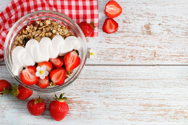 bowl of oat granola with yogurt, fresh strawberry and nuts on white wooden board for healthy breakfast. top view with copy space stock photo