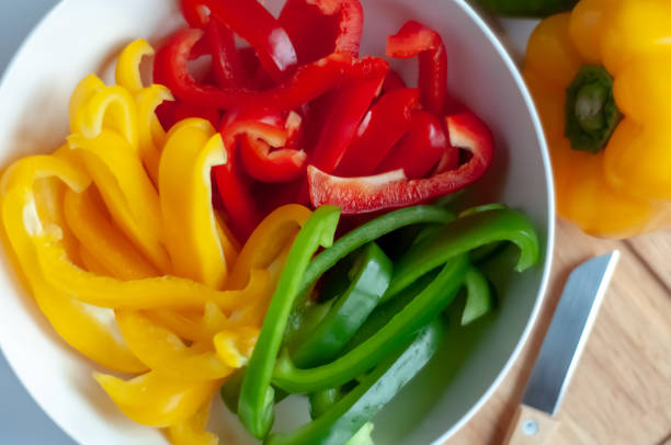Bowl of Sliced Bell Peppers Bowl of sliced yellow, red and green bell peppers with whole peppers and paring knife on wooden cutting board. bell pepper stock pictures, royalty-free photos & images