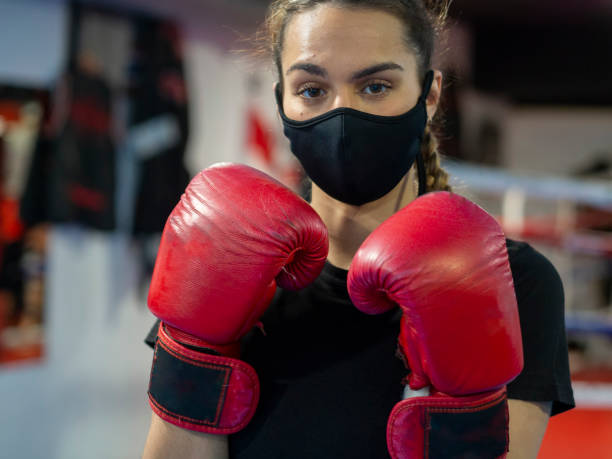 Boxer girl wearing a mask and red boxing gloves in a gym stock photo