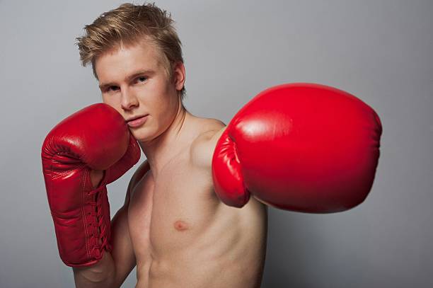 boxer hits Portrait of a young blond man with boxing gloves against grey background teenage boys men blond hair muscular build stock pictures, royalty-free photos & images
