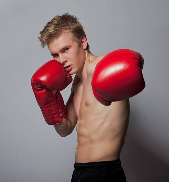 boxer with gloves Portrait of a young blond man with boxing gloves against grey background teenage boys men blond hair muscular build stock pictures, royalty-free photos & images