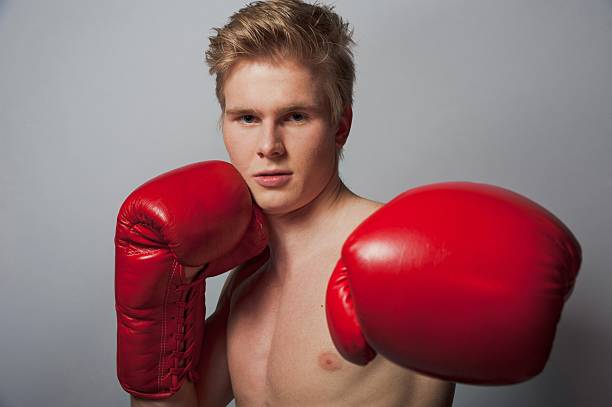 boxer with red gloves Portrait of a young blond man with boxing gloves against grey background teenage boys men blond hair muscular build stock pictures, royalty-free photos & images