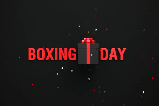 Boxing Day text and black gift box sitting behind gold colored confetti over black background. Horizontal composition with copy space. Directly above. Great use for Boxing Day concepts.