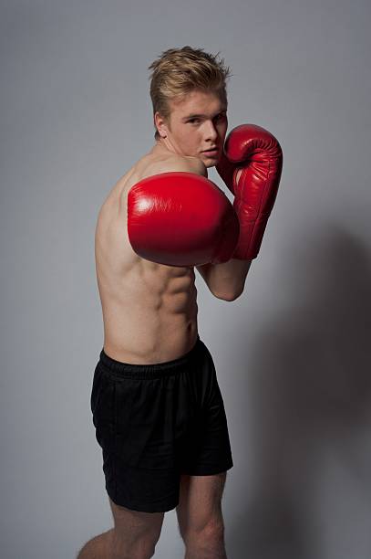 boxing Portrait of a young blond man with boxing gloves against grey background teenage boys men blond hair muscular build stock pictures, royalty-free photos & images