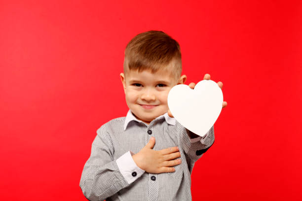 Boy 4 years old holds a white heart of paper stock photo