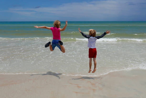Boy and girl jumping in ocean waves stock photo