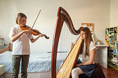 Boy and girl playing harp and violin at home. They are practicing playing their instruments together.
Photo taken during quarantine because of corona virus outbreak.