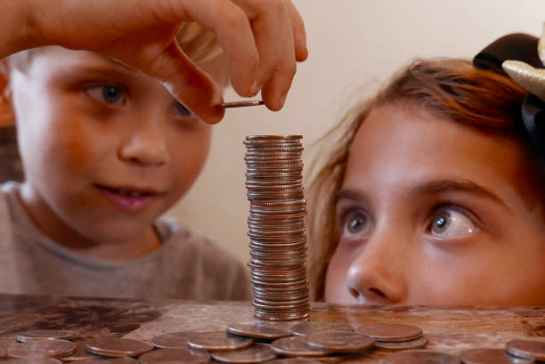 Boy and girl stacking coins on a table stock photo