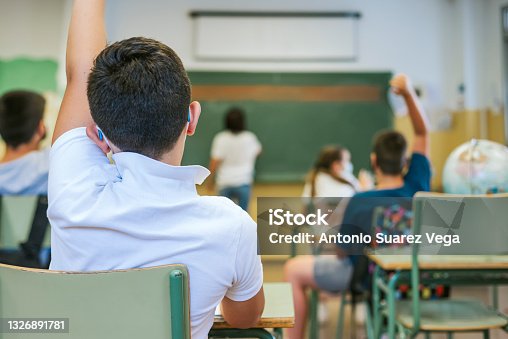 istock A boy and his classmates raise their hands as the teacher writes on the blackboard. Back to school concept 1326891781