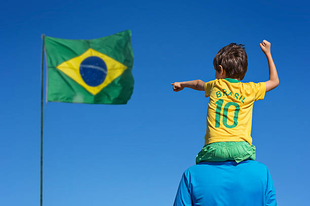 Boy and his father looking up at the Brazilian flag. Boy and his father looking up at the Brazilian flag, Blue sky. brazilian culture stock pictures, royalty-free photos & images