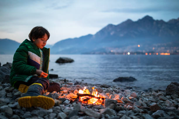 Boy and small bonfire near the shore of the lake stock photo