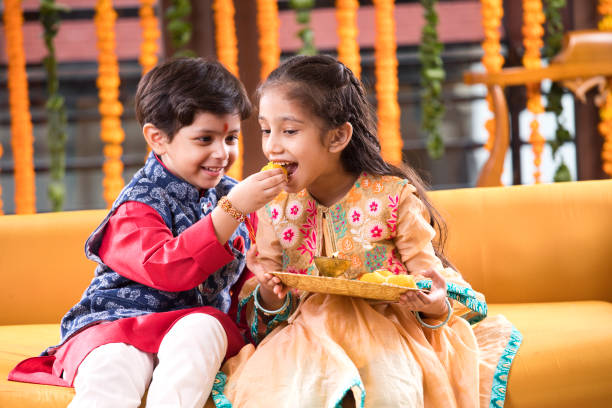 Little brother feeding sweet food to his sister on the occasion of Raksha Bandhan festival