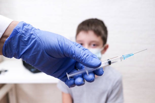 A boy getting vaccinated from covid-19, a doctor hold a syringe in order to vaccinate a teenager stock photo