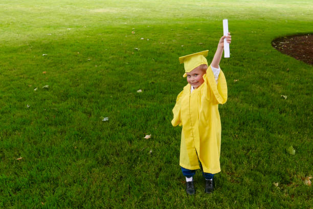 Boy graduating from preschool holds up his diploma stock photo