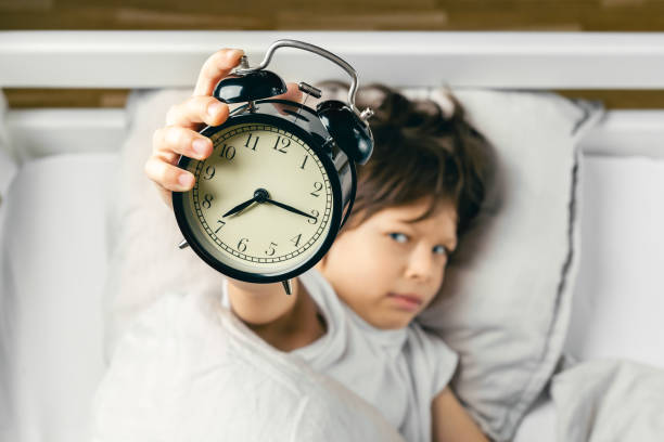 Boy holding alarm clock showing quarter past seven stock photo