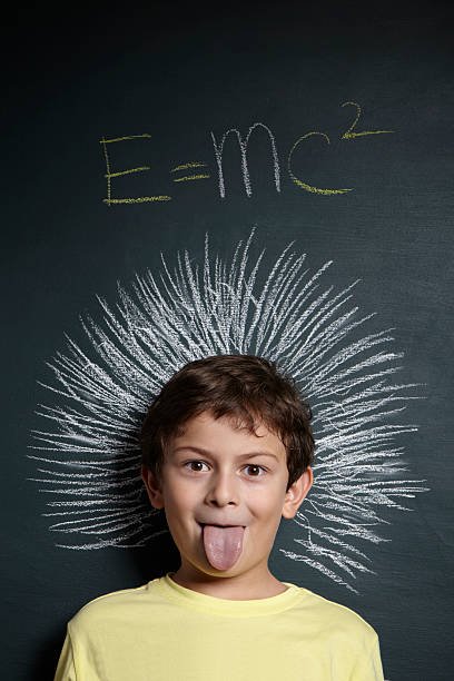 Boy imitating Einstein photo in front of chalkboard Little boy in front of blackboard E=mc2 written on it. e=mc2 stock pictures, royalty-free photos & images