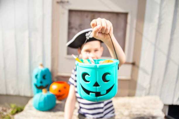 boy in a pirate costume holds a bucket with inedible gifts Teal Pumpkin Project. Alternative non-food treats for kids with food allergies. the concept of health for children in the Halloween season. teal stock pictures, royalty-free photos & images
