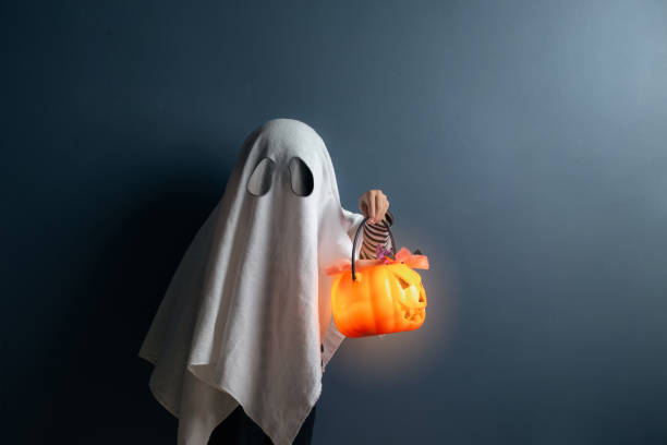 A boy in ghost costume hold a pumpkin head basket with candy at the halloween night.  ghost boy stock pictures, royalty-free photos & images
