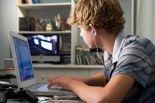 boy in his bedroom using his laptop wearing earphones - alleen één tienerjongen stockfoto's en -beelden