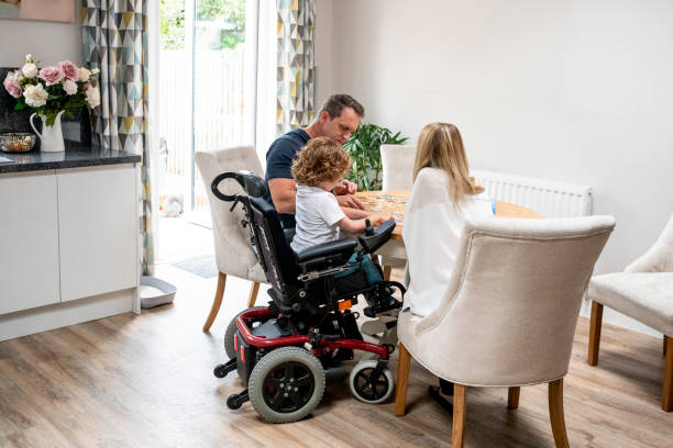 Boy in wheelchair doing jigsaw with parents 6 year old boy with muscular dystrophy, sitting at dining table with mother and father, playing a game, quality time with family physical disability stock pictures, royalty-free photos & images