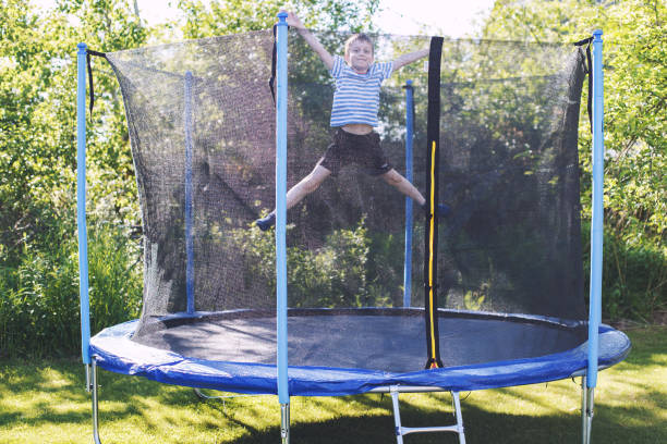 ragazzo che salta sul trampolino. il bambino gioca su un trampolino all'aperto - tappeto elastico foto e immagini stock