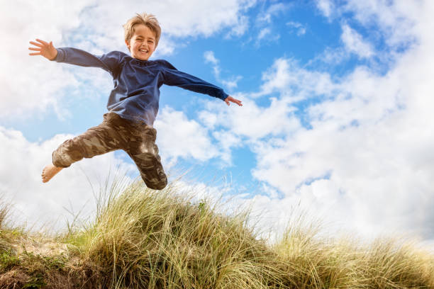 Boy leaping and jumping over sand dunes on beach vacation Boy jumping over sand dunes on beach vacation exhilaration stock pictures, royalty-free photos & images