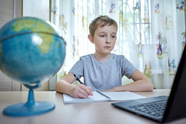 A boy looks at a laptop while doing homework stock photo