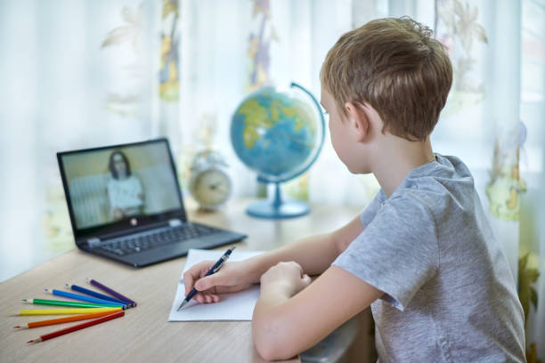 A boy looks at a laptop while doing homework stock photo