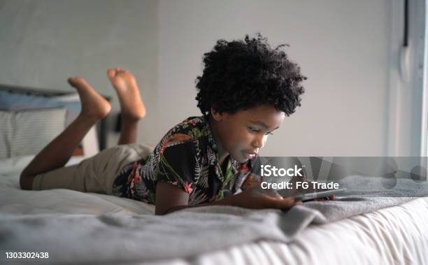 Boy lying in bed playing games on digital tablet at home