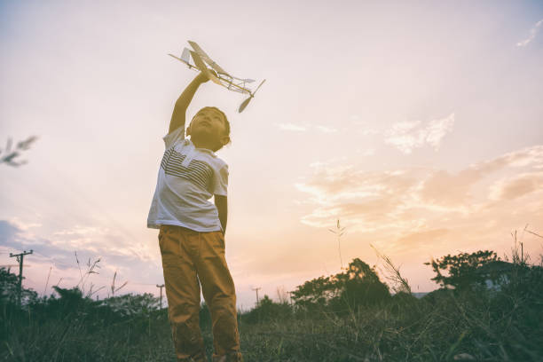 boy playing airplane toy in field stock photo