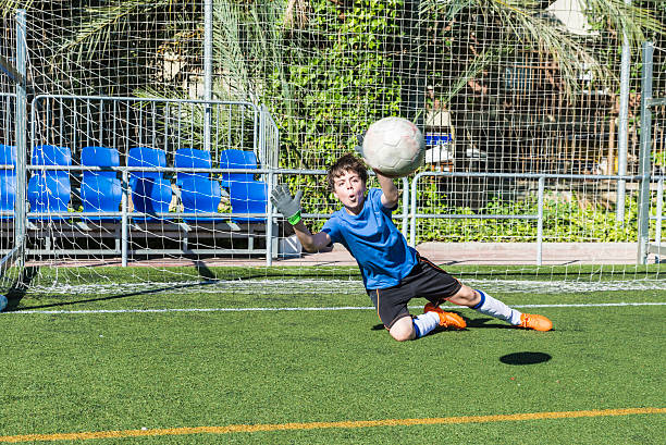 Boy playing soccer goalie Young football goalkeeper stretching to stop a ball goalie stock pictures, royalty-free photos & images