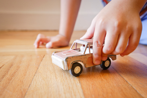This is a nostalgic image of a young boy playing with an antique toy SUV on a wood floor.