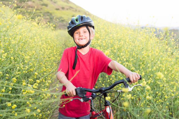 Boy Posing With Mountain Bike In Wild Flowers A 6 year old boy smiling at the camera surrounded by beautiful wild flowers. lake hodges stock pictures, royalty-free photos & images