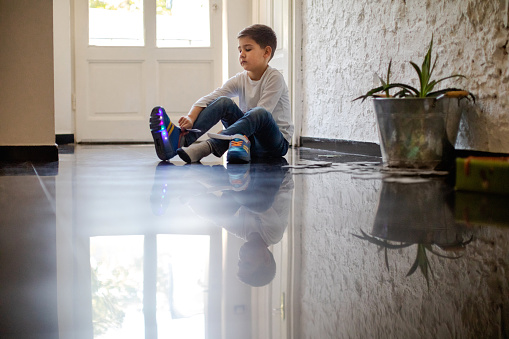 Boy sitting on the floor at home and putting on sports shoes with LED illumination