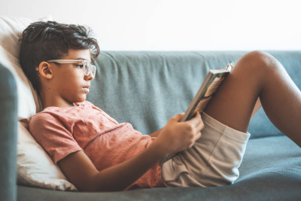 boy reading book on sofa - child reading imagens e fotografias de stock