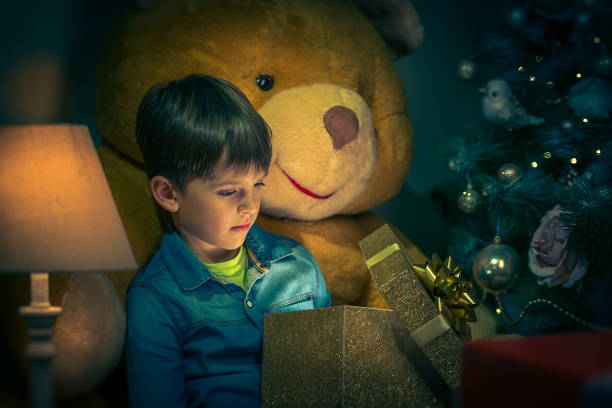 A boy reads a book in front of a New Year’s spruce with New Year’s gifts stock photo