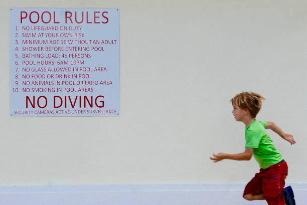 Boy running by a "pool rules" sign stock photo