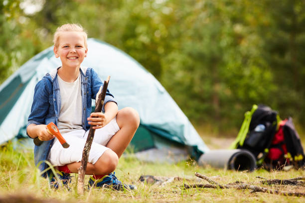 Boy scout Cheerful boyscout with axe and stick looking at camera while enjoying trip on summer day boy scout camping stock pictures, royalty-free photos & images