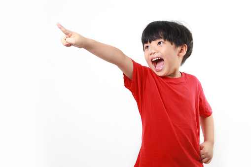 Studio shot of little Asian boy pointing, shouting and looking up, isolated on white background