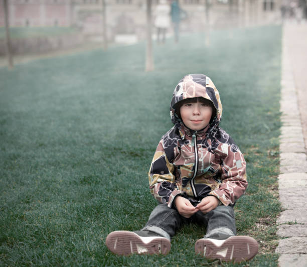 Boy sits on grass in the park, fall season stock photo