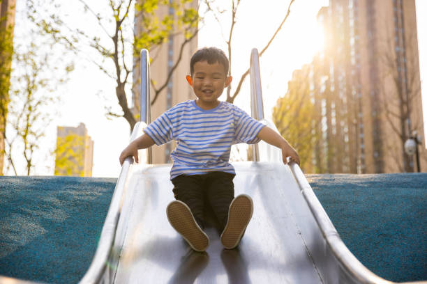 Boy sliding down  in an outdoor play park stock photo