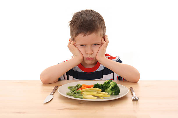 A boy sulking as he doesn't want to eat the vegetables stock photo