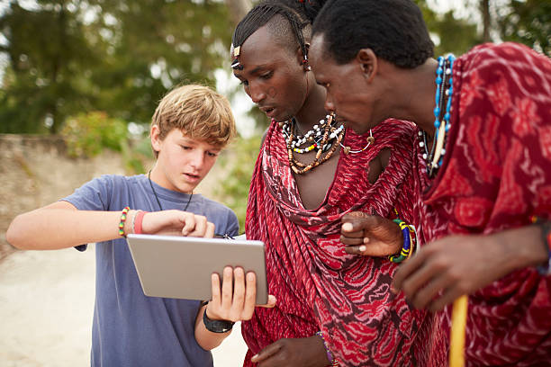 Boy teaching Maasai warriors to use a digital tablet. Boy teaching Maasai warriors to use a digital tablet. maasai warrior stock pictures, royalty-free photos & images