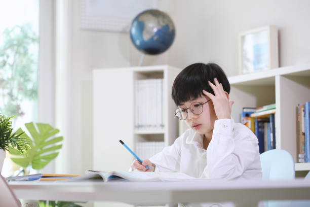 Boy thinking carefully, concentrating and studying hard at his desk Smart and cute student thinking carefully, concentrating and studying hard, taking notes in books and notes at his desk, learning. maths stock pictures, royalty-free photos & images