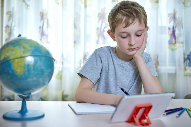 Boy thinks while doing homework at home stock photo