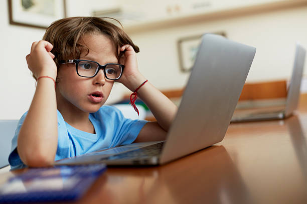 Boy using laptop at table Little boy using laptop at table in house boys glasses stock pictures, royalty-free photos & images