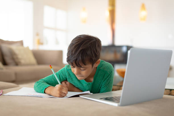 jongen met behulp van laptop tijdens het tekenen van een schets op boek thuis - huiswerk stockfoto's en -beelden